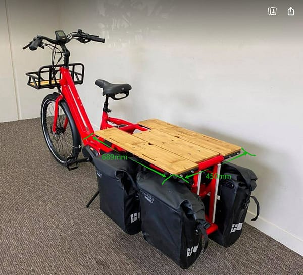 Rød elektrisk lastesykkel med doble batterier med utbygd lasteplan og sidevesker.